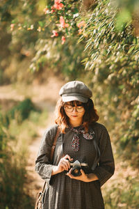 Young woman wearing hat standing against plants