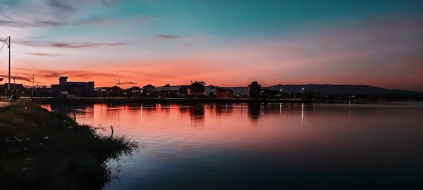 Silhouette buildings by lake against sky during sunset