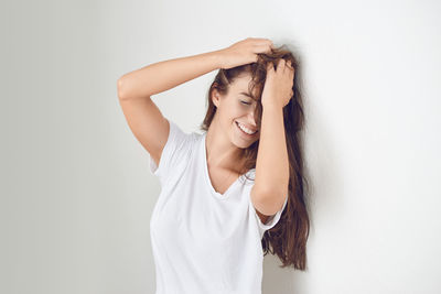 Smiling young woman with hand in hair against white wall