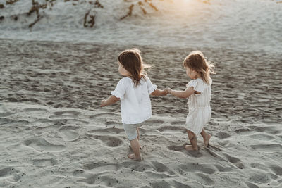 Side view of young toddler girls holding hands and walking at beach