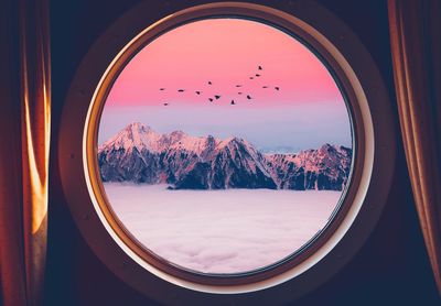 Snowcapped mountains and clouds seen through circle shaped window