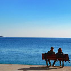 Rear view of couple sitting at beach against clear sky