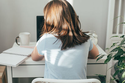 Rear view of woman using laptop at home