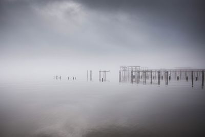 Wooden posts in sea against sky