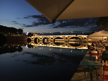 Illuminated bridge over river against sky at sunset