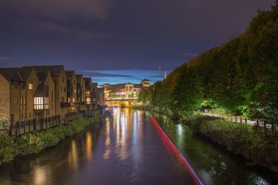 River amidst illuminated houses against sky at night