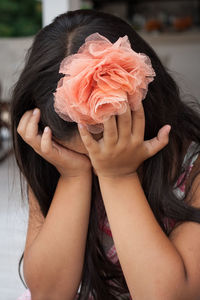Sad girl wearing artificial flower while covering eyes with hands