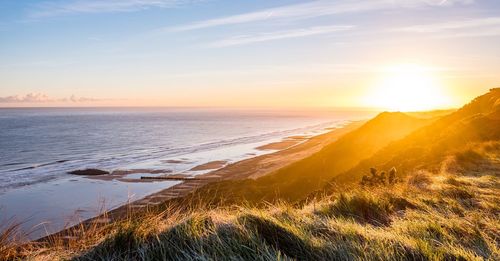 Scenic view of mountains by sea against sky during sunset