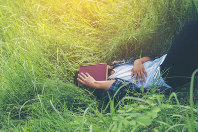 Man covering face with book while lying on grassy field