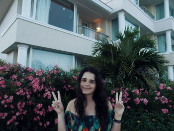 Portrait of smiling woman gesturing peace sign against flowering plants