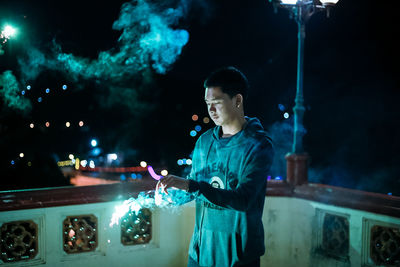 Young man holding sparkler at balcony during night