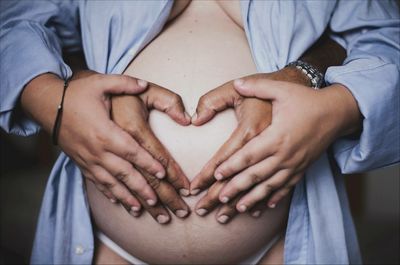 Midsection of pregnant woman with man making heart shape on belly