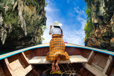 Rear view of woman sitting by sea against sky