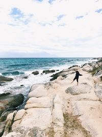 Man standing on rock at sea shore against sky