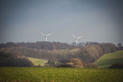 Wind turbines on field against sky