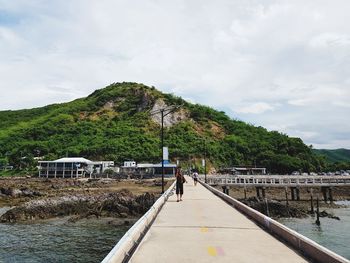 People walking on bridge over sea against mountain