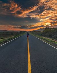 Rear view of man walking on road during sunset