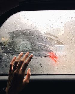 Cropped image of hand touching wet car window