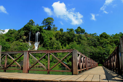 Footbridge amidst trees against blue sky