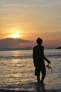 Silhouette man standing on sea against orange sky