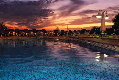 Silhouette people by swimming pool against sky during sunset