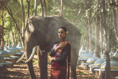 Smiling woman standing with elephant in forest