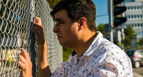 Sad teary caucasian man holding fence. profile view. portrait.