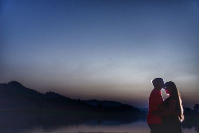 Side view of couple standing by lake against clear sky