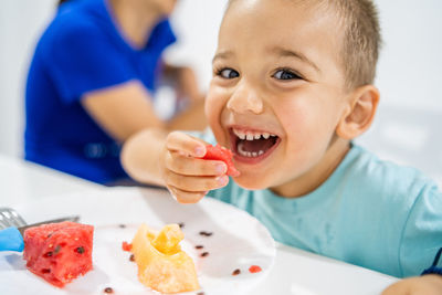 Close-up portrait of cute boy eating fruit in plate on table