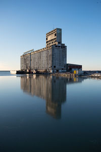 Reflection of building in sea against clear blue sky