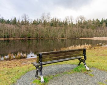 Bench by lake against sky