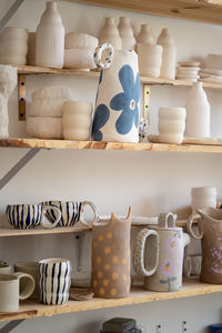 Handmade ceramic cups, jugs, jars and vase on shelves in craft pottery kitchenware store or workshop