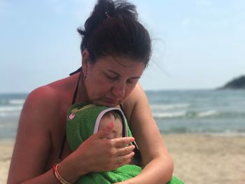 Grandmother with baby sitting at beach against sky