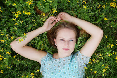 Portrait of young woman lying on grassy field with flowers