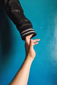 Cropped hand of person touching jacket sleeve against blue wall