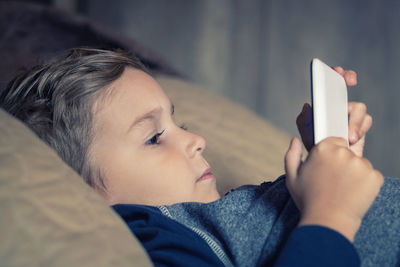 Boy using mobile phone while lying down on bed at home