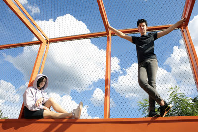 Full length of young man with arms raised against sky