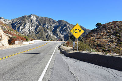 Road sign by mountains against clear sky