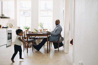 Father working on laptop while daughter playing in kitchen