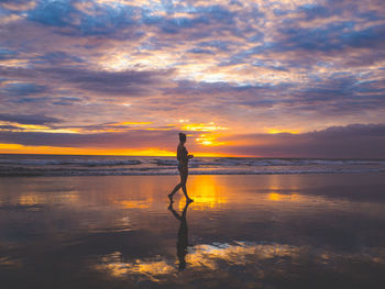 Man standing in sea against dramatic sky during sunset