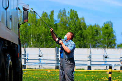 Side view of man wearing mask cleaning truck