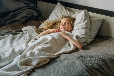 Happy child lies on the bed under a white blanket on the pillow sleep