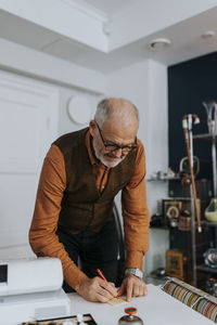 Senior male owner writing on paper at desk while working in antique shop