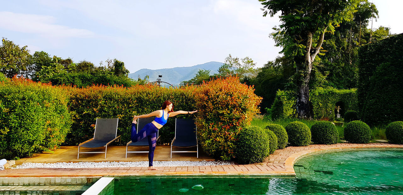 WOMAN IN SWIMMING POOL AGAINST PLANTS