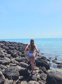 Rear view of woman wearing bikini walking at beach against clear sky