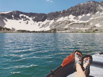 Low section of person relaxing on boat in lake near snowcapped mountain