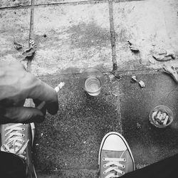 Low section of man holding cigarette by drink on sidewalk