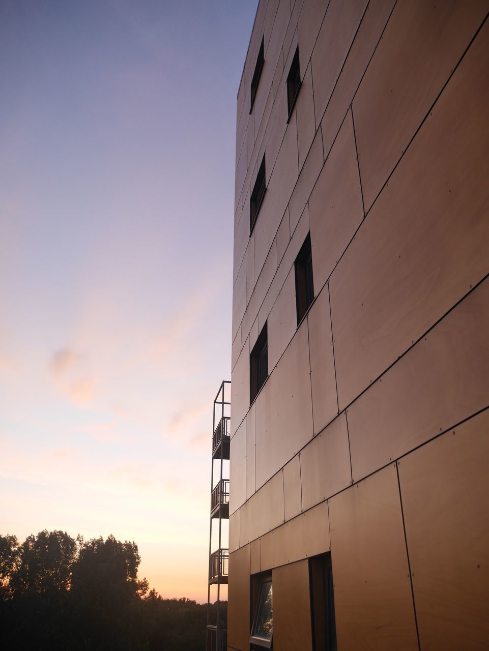 building exterior, architecture, built structure, low angle view, sky, sunset, city, building, tree, power line, tall - high, silhouette, outdoors, tower, no people, modern, office building, residential building, orange color, residential structure