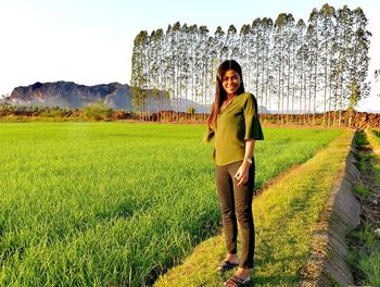 Full length portrait of smiling woman standing on field