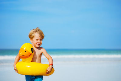 Portrait of boy playing with arms raised on beach against sky